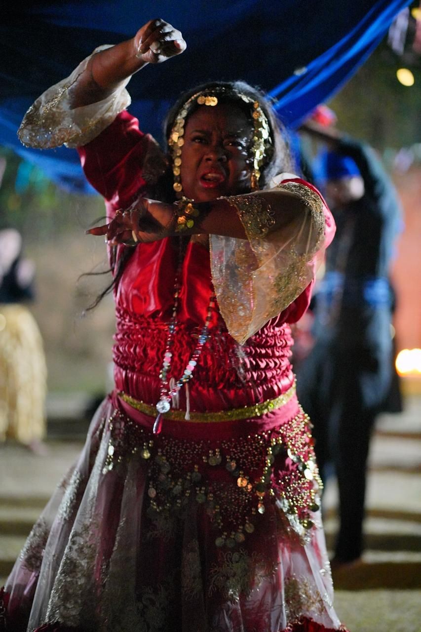 Person dressed in traditional attire with red and gold embellishments dancing energetically under a blue canopy.
